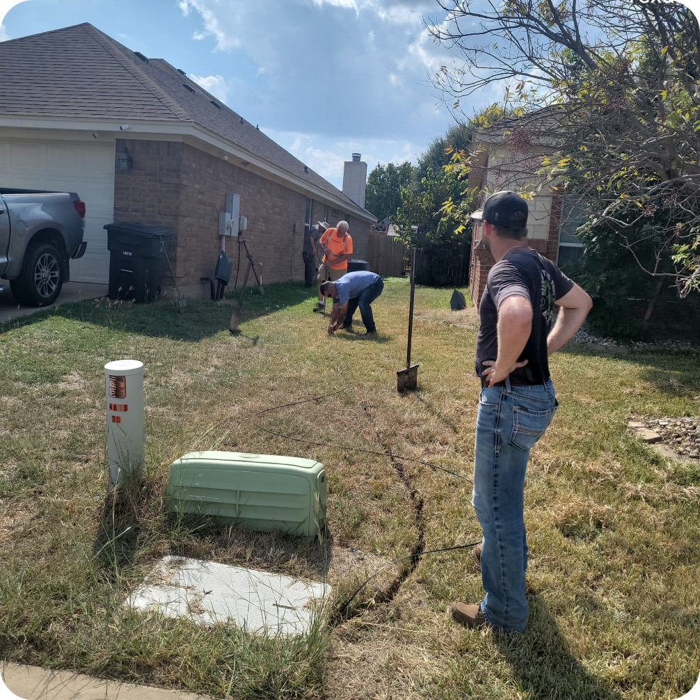 Brightspeed technicians installing a direct fiber line outside a residential home, digging a small trench from the street to the house to enable reliable high-speed internet and fiber connectivity.
