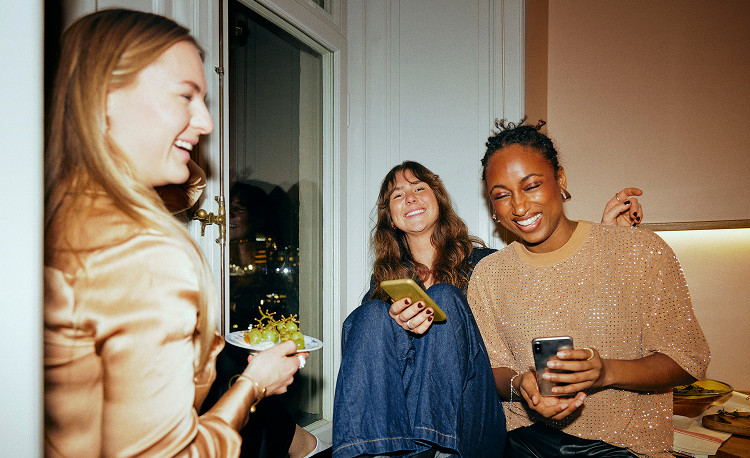 Friends gathering at home and using smartphones, staying connected with Brightspeed Internet.