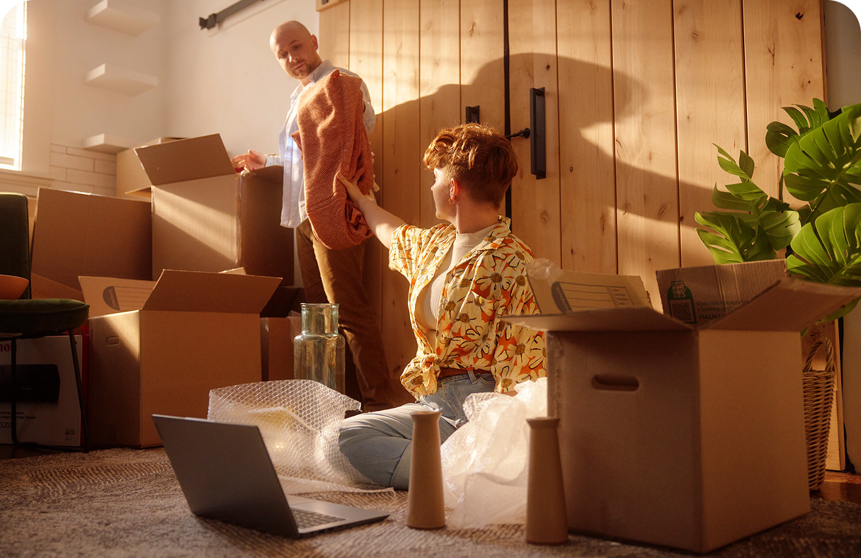 Two people packing and unpacking boxes in a sunlit home while setting up Brightspeed internet on a laptop.