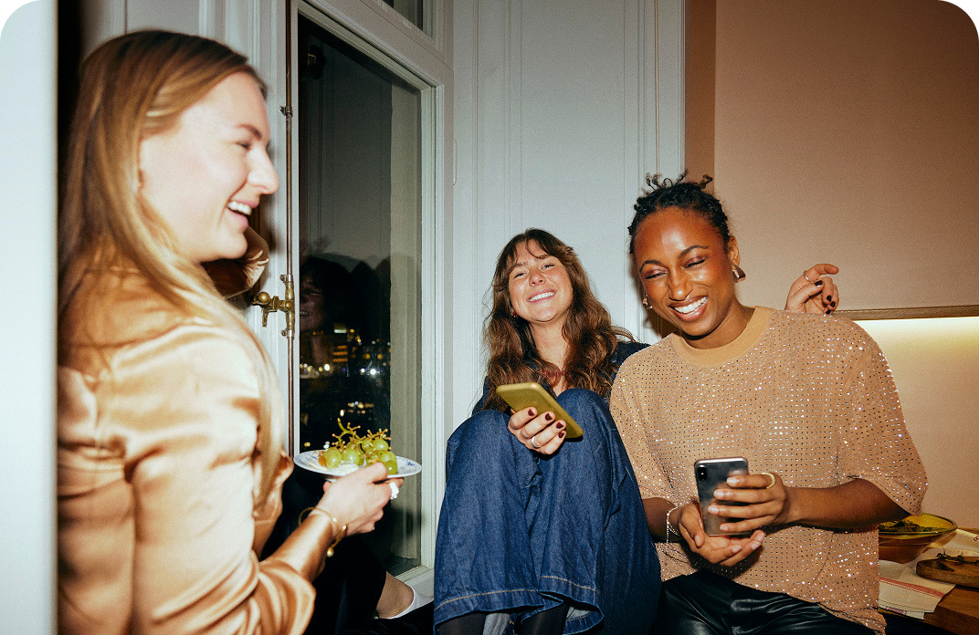 Three friends enjoying time together at home while using mobile devices, powered by Brightspeed Internet.