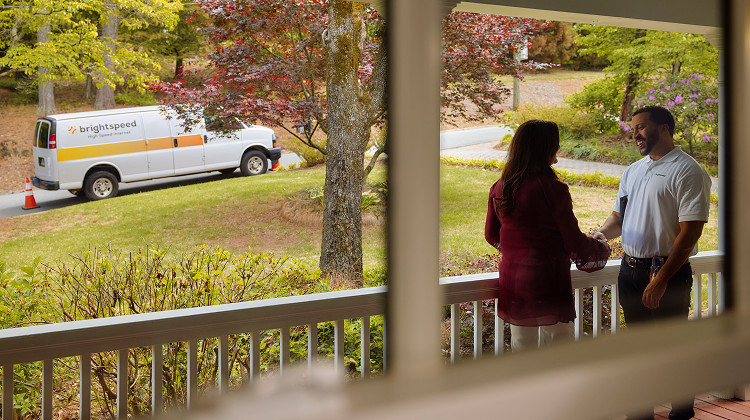A young lady and young man standing in balcony area talking to each other.